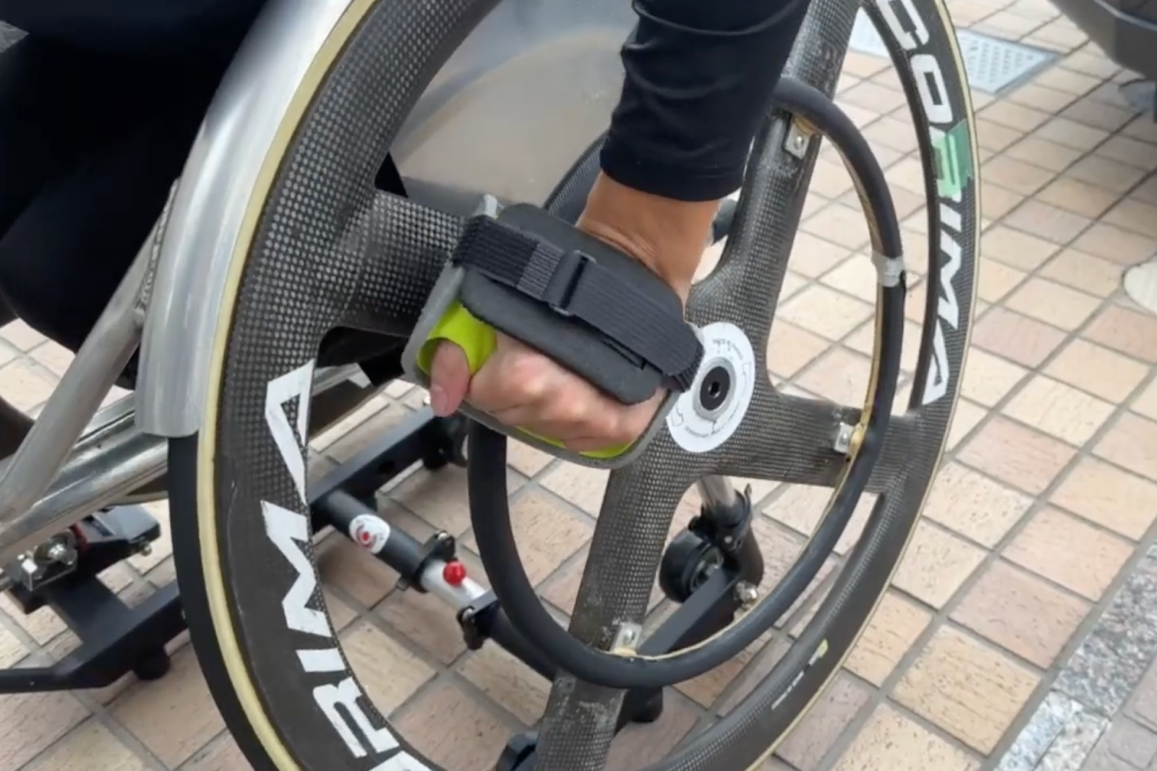 車いす陸上選手が、専用グローブを装着して後輪のハンドリムを押す様子です。選手一人ひとりの身体や走り方に合ったグローブをつくるために、実際の使用感や選手の声を大切にしています。